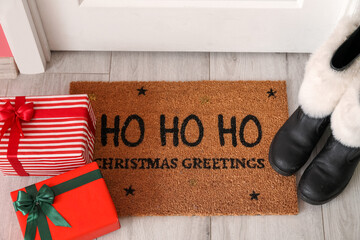 Santa Claus shoes, gift boxes and floor mat with Christmas greetings near white door
