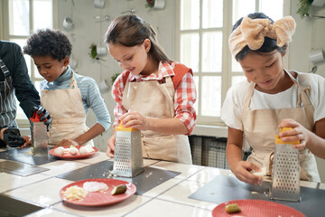 Group of children standing at the table and learning to cook during masterclass with the chef