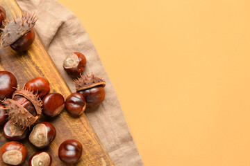 Wooden board with chestnuts on color background, closeup