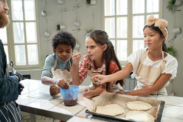 Group of children tasting sweet cream, they baking homemade cookies together during a lesson