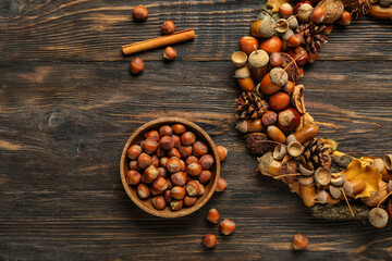 Bowl with hazelnuts and beautiful acorn wreath on wooden background