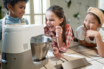 Group of children having fun during cooking, they making cream with mixer at the table in the kitchen