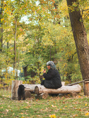 grey haired caucasian woman walking a black dog in the forest in autumn