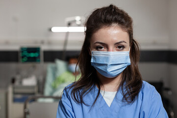 Portrait of practitioner nurse wearing protective face mask to prevent infection with coronavirus looking into camera during medical appointment working in hospital ward. Medicine services