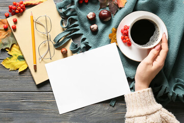 Female hand with cup of coffee, blank sheet of paper, eyeglasses and autumn decor on dark wooden background, closeup