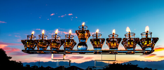 Crystal festive menorah and burning candles with olive oil as symbol of Hanukkah - Jewish Holiday of Miracle Light. Blurred background of mountains and dramatic sky cloud at sunset 