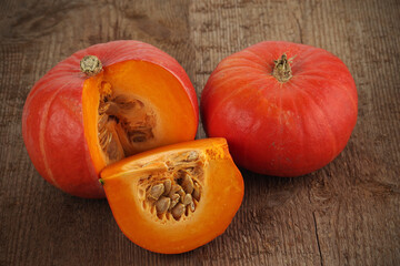 Two red kuri squash, whole and cut, on a rough woody texture background. Selective focus.