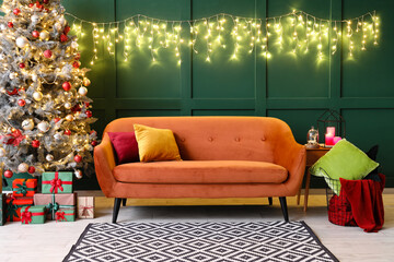 Red sofa with Christmas tree, gifts and glowing lights near green wall