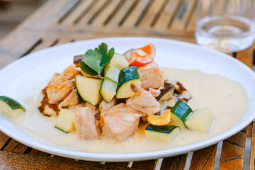 Salmon and vegetable dish with cream sauce on a plate, wooden table, outside