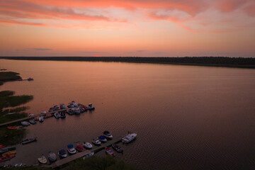Fototapeta premium Sunset over the lake. Orange clouds during summer sunset. Motorboats docked at the marina.