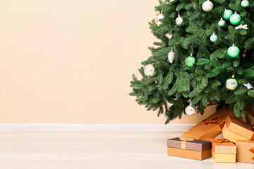 Fototapeta premium Beautiful Christmas tree with gift boxes near beige wall