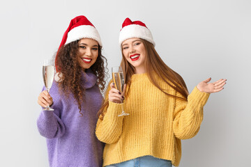 Beautiful young women in Santa hats and with glasses of champagne on light background