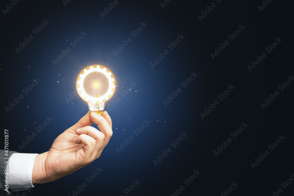 Poster close up of businessman hand holding lamp with glowing cogwheel on blue background with mock up plac