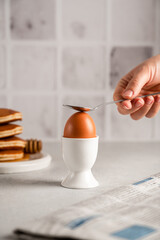 A woman's hand breaks eggshells with a spoon for breakfast in the white kitchen at home