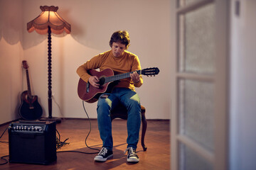 Male musician playing acoustic guitar on the amplifier in retro vintage room.