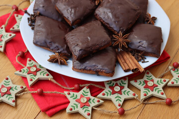 Italian traditional festive cookies called Mostaccioli or Mustaccioli on a plate on red napkin with festive decorations on wooden table. Christmas cookies made mith Pisto, a mix of various spices