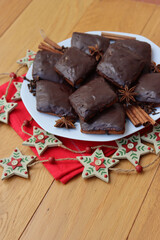Italian traditional festive cookies called Mostaccioli or Mustaccioli on a plate on red napkin with festive decorations on wooden table. Christmas cookies made mith Pisto, a mix of various spices