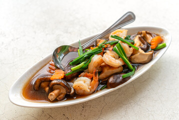 Stir-fried shrimps, Shiitake mushrooms, or Chinese mushrooms with oyster sauce in beautiful oval-shaped plate on the white stone table, close up image of healthy Thailand food menu.