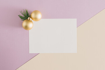 Christmas and New Year festive idea with golden baubles, green fir and white paper card. Pastel violet and beige background with copy space. Creative minimal flat lay winter holiday design.