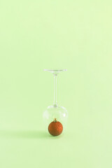 Christmas and New Year decoration idea with a drinking glass and red bauble on pastel bright green background. Creative holiday party and winter concept, minimal vertical aesthetic composition.