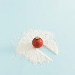 Winter decoration concept with red bauble and snow on bright blue background. Creative Christmas and New Year decoration idea, minimal aesthetic arrangement.