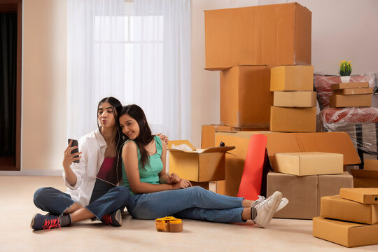 Adult girls listening music and taking selfie while sitting on floor during leisure time