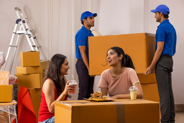 Adult girls eating pizza while the delivery boys moving cardboard boxes