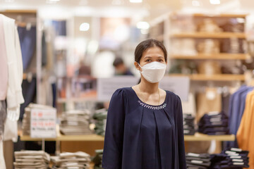 Adult woman in medical mask in a store. Buying clothing at the supermarket. Visiting public places during the coronavirus pandemic