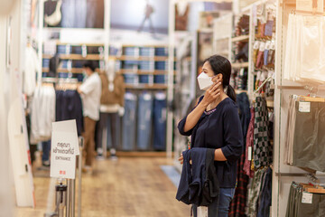 Adult woman in medical mask in a store. Buying clothing at the supermarket. Visiting public places during the coronavirus pandemic