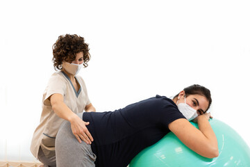 A pregnant woman doing pilates exercises with a ball with the help of her physiotherapist