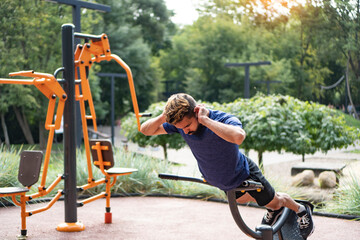 Hyperextension exercise. Charismatic man trains at the open air gym. Outdoor fitness background.