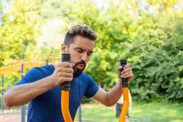 Open air gym. Cardio workout. Athletic man is jogging on outdoor orbitrack machine. Street training on the municipal sports simulators.