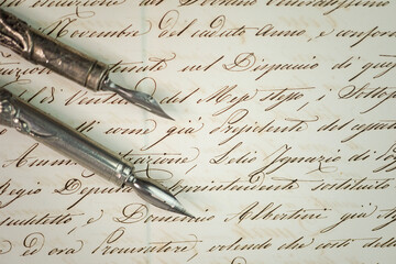 Two old steel penholders with calligraphy nibs over a writing sample