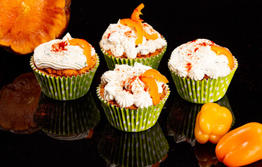 Pumpkin muffin in green cups with pepper and pumpkin on background, cream decoration