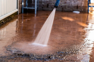 Cleaning dirty backyard paving tiles with pressure washer cleaner.