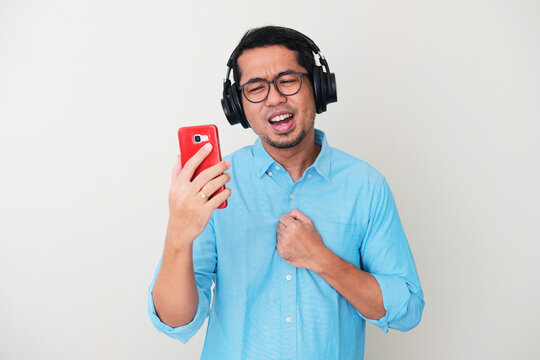 Adult Asian man wearing headset singing a song while read the lyric on his mobile phone