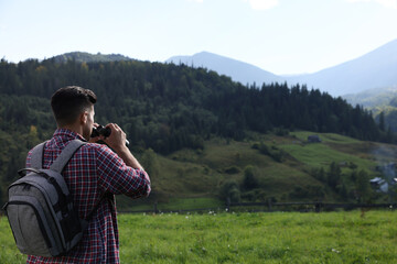 Tourist with backpack and binoculars enjoying landscape in mountains, back view