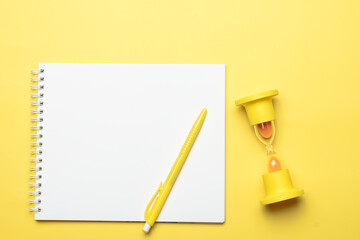 top view with white sheet of paper in a notebook with objects for office work, pen and yellow hourglass, all yellow objects on a yellow background monochrome flat lay
