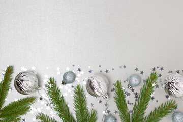 Border frame made of Christmas decorations and fir tree branches on a silver background.