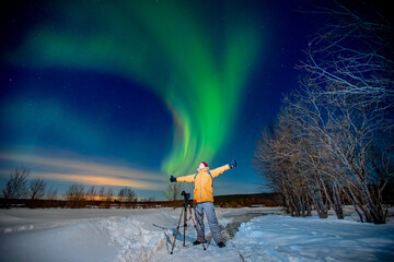 Photographer man with camera and tripod photographs aurora borealis, northern lights green. Concept photo tour to arctic travel © Parilov