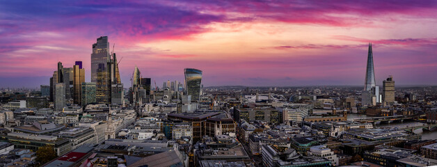 Wide panoramic aerial view of the 2021 skyline of London, England, with the City skyscrapers, Tower Bridge and river Thames during a colorful dusk