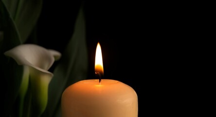 Candle burning flame in the darkness and arum lilies