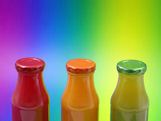 glass bottles with healthy smoothies on multicolored background with copy space, close up of red, orange and green fuit juice bottles