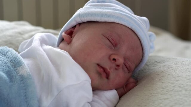 Close-up Newborn Baby Face Portrait Early Days Sleeping Sweetly On Tummy Blue White Background. Child At Start Minutes Of Life on Hat. Infants, Childbirth, First Moments Of Borning, Beginning Concept