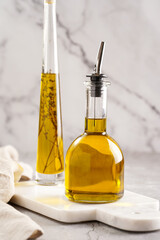 Two bottles with olive oil and fresh herbs - thyme - on white marble background