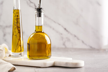 Two bottles with olive oil and fresh herbs - thyme - on white marble background