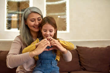 Aged woman teaching little heart to make heart sign