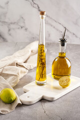 Two bottles with olive oil and fresh herbs - thyme - on white marble background