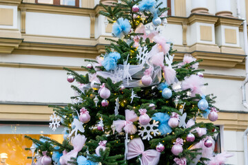 Fototapeta na wymiar Beautiful Christmas tree on a city street. Blue and pink tulle bows, balls, snowflakes and ballerinas as decorations on the fir tree.