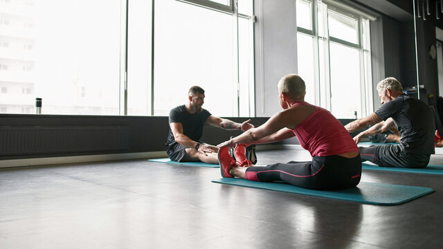 Male trainer assisting senior couple in performing stretching in gym